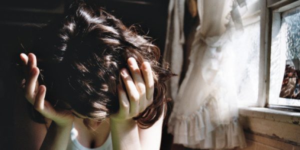 Girl with hand on head sitting near window