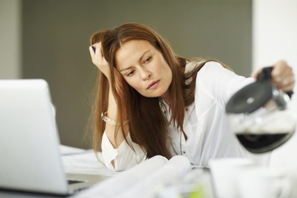 Tired female architect pouring coffee while working