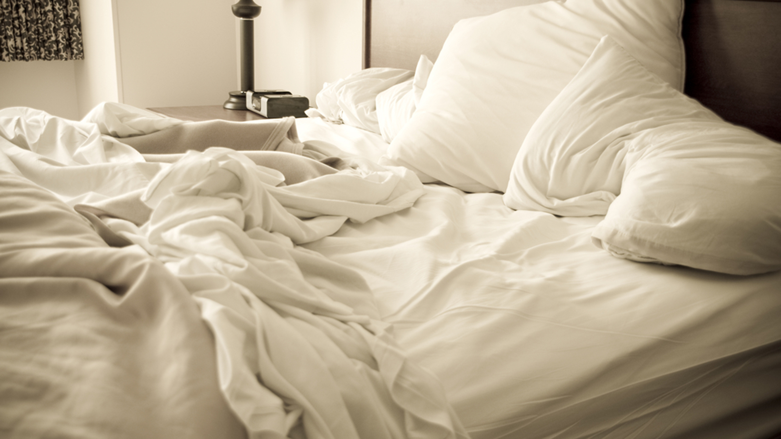 An unmade bed with white linens and a lamp in the corner.; Shutterstock ID 197136716; PO: MC for TODAY
