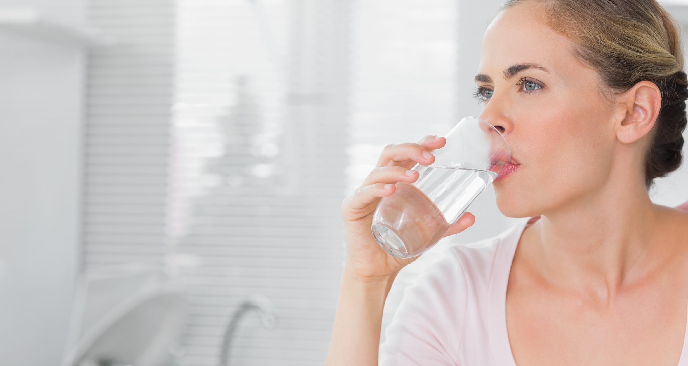 Pensive blond woman drinking water in her kitchen