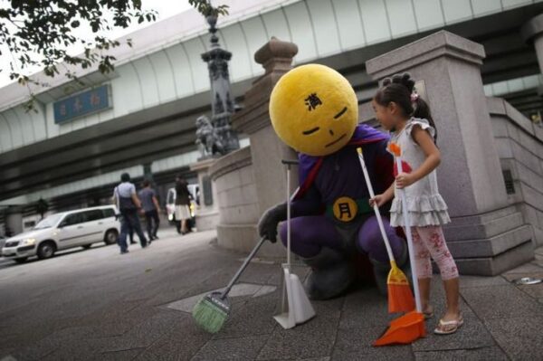 An unidentified man, who calls himself Mangetsu-man (Mr. Full Moon),  pauses as he cleans Nihonbashi bridge using a broom with a volunteer in Tokyo