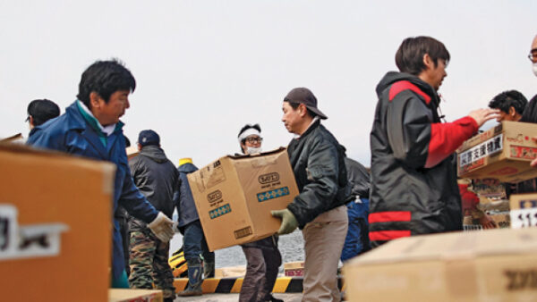 People unload aid from a small ship at the devastated port of the island of Oshima