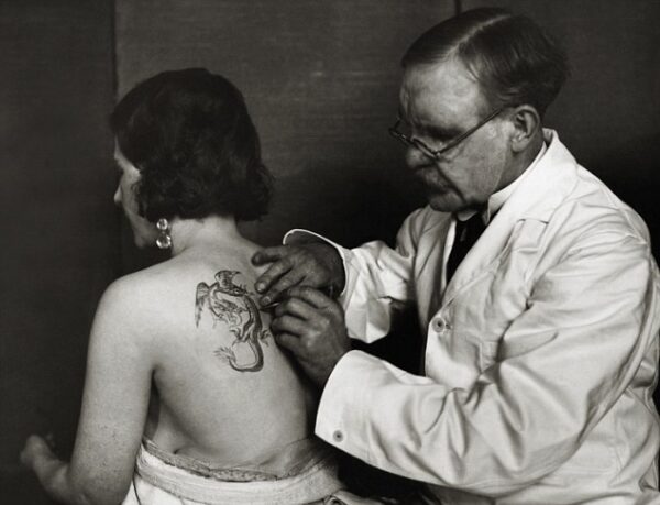 ca. 1930, England, UK --- Tattoo Artist Tattoos Woman --- Image by © E.O. Hoppé/CORBIS
