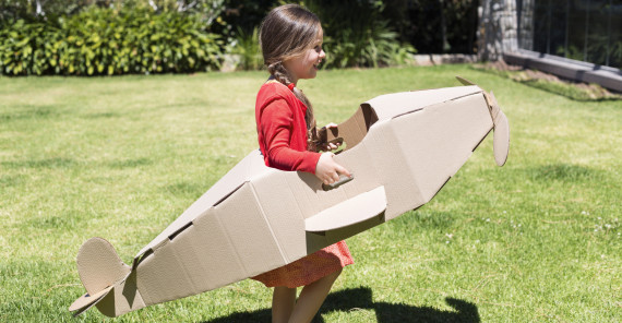 Girl playing with a cardboard airplane in lawn