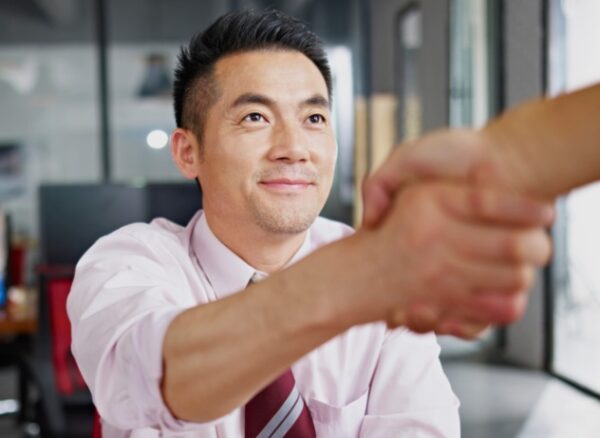 asian businessman shaking hands with visitor in office.