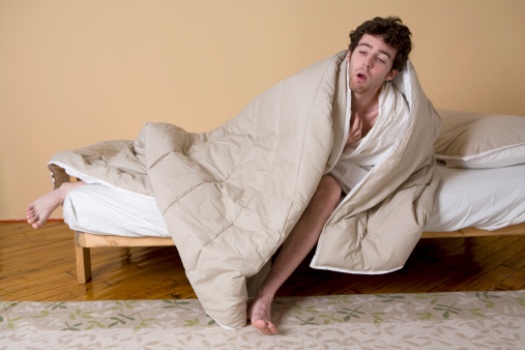 Young man wrapped in blanket on edge of bed
