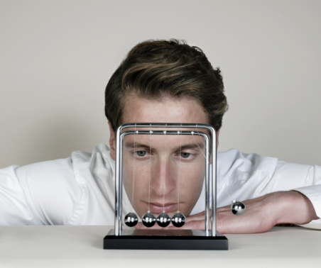 Businessman looking closely at Newton's Cradle