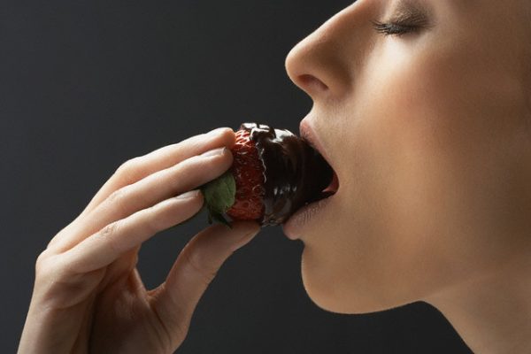 Woman bitting chocolate covered strawberry --- Image by © Paul Taylor/Corbis