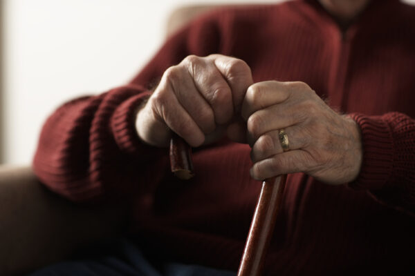 Senior man holding cane, mid section, close-up of hands