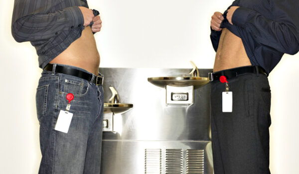 Two men lifting shirts beside drinking fountains, mid section