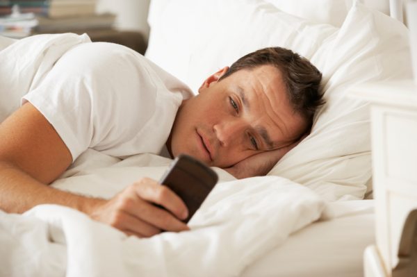 Man In Bed At Home Texting On Mobile Phone