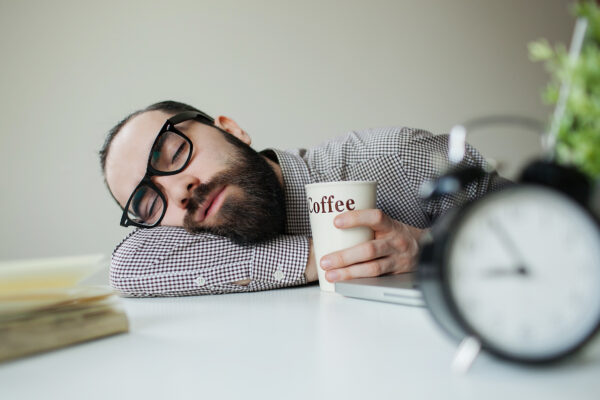 Man sleeps on office table over laptop with coffee