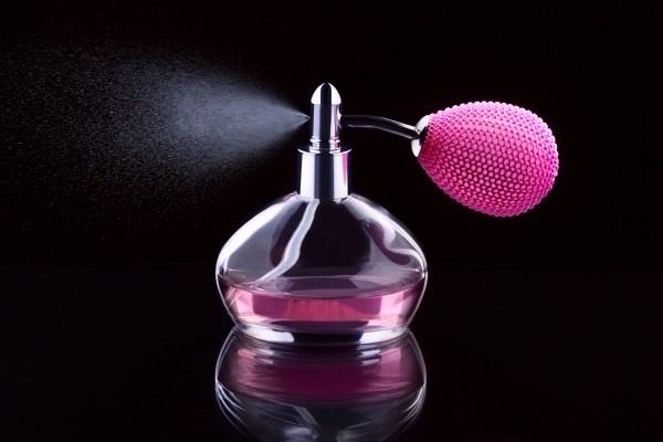 Pink bottle of perfume spraying; isolated on black background