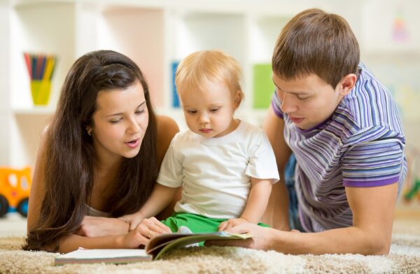 Young happy family with baby boy read children book laying on floor