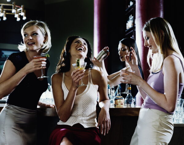 Three young women drinking cocktails at bar, laughing