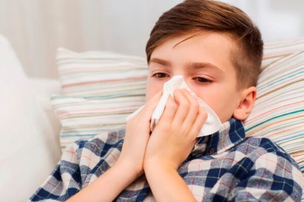 childhood, healthcare, rhinitis, people and medicine concept - ill boy with flu lying in bed and blowing his nose at home