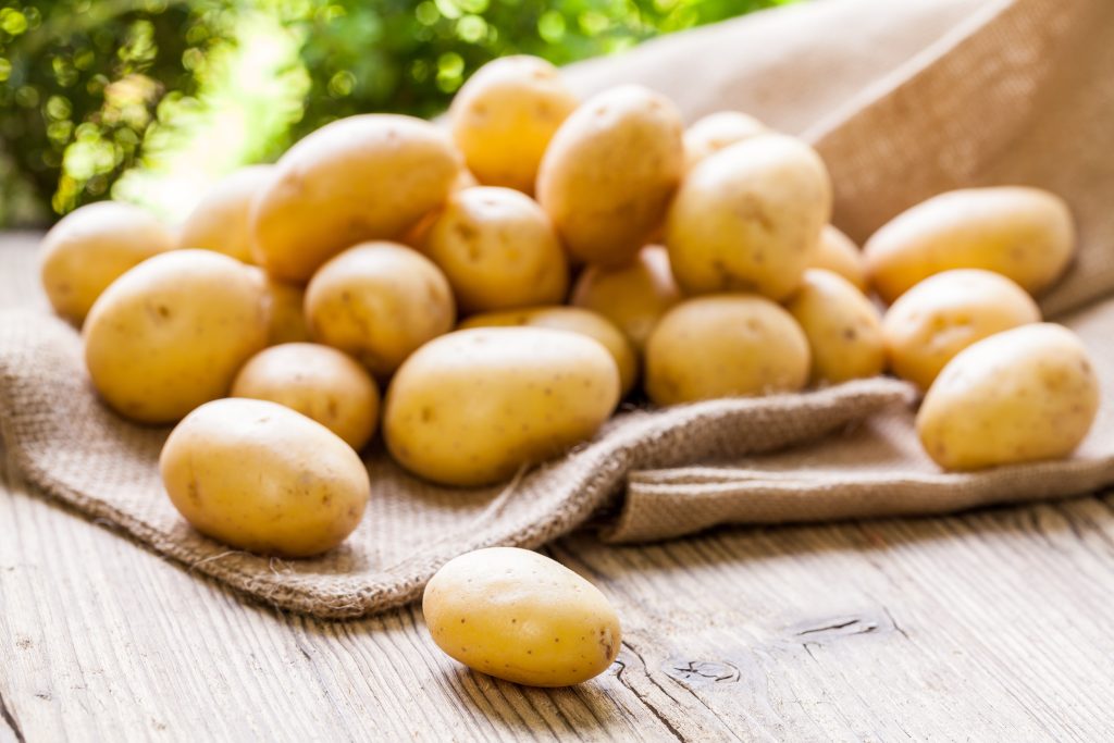 Farm fresh baby potatoes displayed on a hessian sack on a rustic wooden table at farmers market a healthy nutritious root vegetable popular in vegetarian and vegan cuisine ** Note: Shallow depth of field