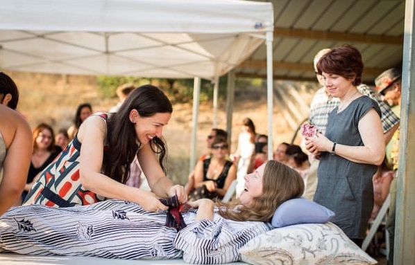 This July 24, 2016 photo provided by Niels Alpert, Amanda Friedland, left, surrounded by friends and family adjusts her friend Betsy Davis's sash as she lays on a bed during her "Right To Die Party" in Ojai, Calif. In early July, Davis emailed her closest friends and family to invite them to a two-day celebration, telling them: "These circumstances are unlike any party you have attended before, requiring emotional stamina, centeredness, and openness. And one rule: No crying." The 41-year-old woman diagnosed with ALS,  held the party to say goodbye before becoming one of the first California residents to take life-ending drugs under a new law that gave such an option to the terminally ill. (Niels Alpert via AP)