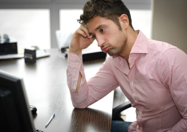 Tired or frustrated young man working in office looking at computer screen