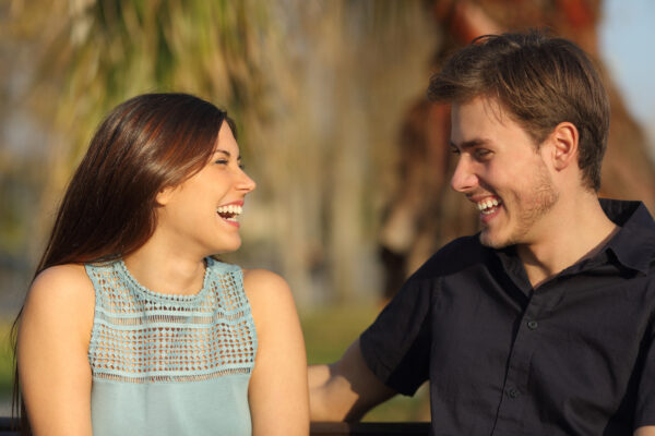 Friends or couple laughing and taking a conversation sitting on a bench in a park