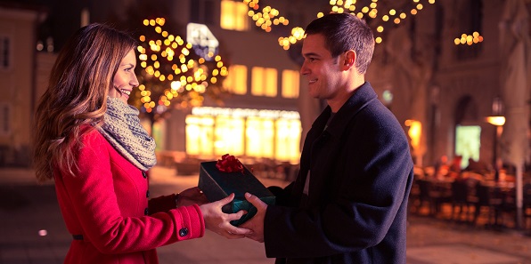 couple holding present looking at each other, young woman receives a gift from her boyfriend