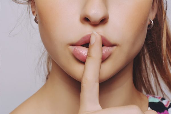 Closeup portrait of beautiful young woman with finger on lips.