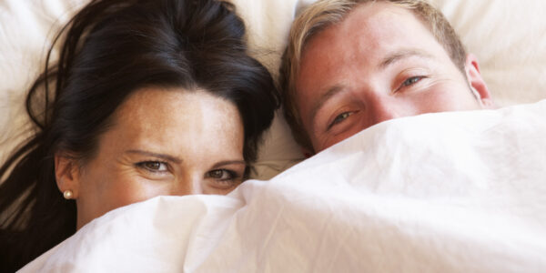 Couple Relaxing In Bed Hiding Under Bedclothes