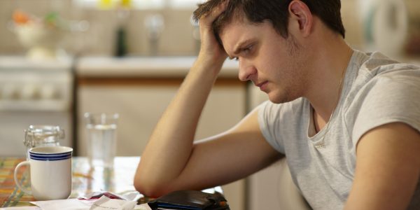 Young man holding head looking at receipts.