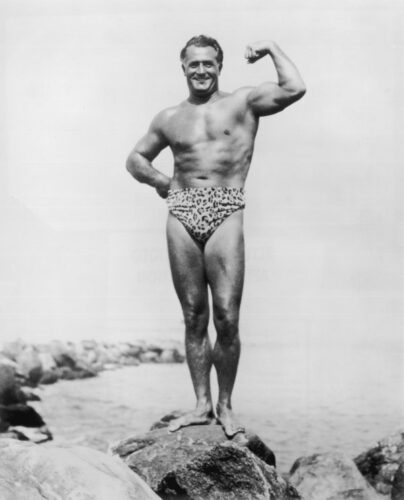 circa 1945: Full-length portrait of Italian-born bodybuilder Charles Atlas (born Angelo Siciliano) (1893 - 1972) flexing his bicep while posing in a leopard print swimsuit on a rock by the water's edge. (Photo by Hulton Archive/Getty Images)