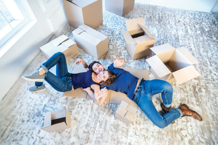 Moving, repairs, new flat. Couple girl and guy lie on the floor in the arms and showing okay thumbs up while man and woman lying on the floor among the boxes in an empty apartment view from above