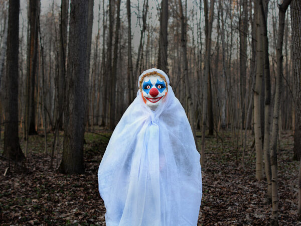 evil clown in a mask standing in a dark forest in a white veil
