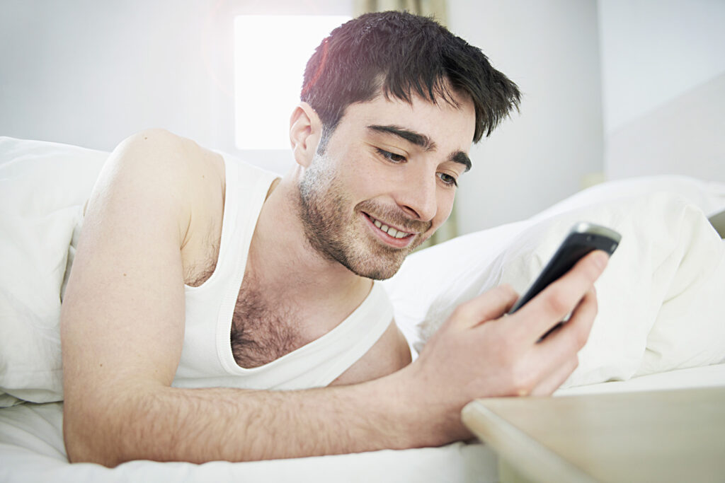 man looking at mobile phone in bed