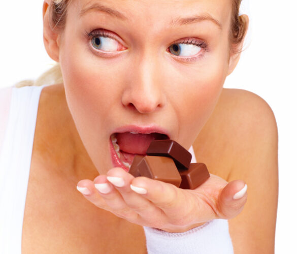 Young cute woman trying to eat chocolates over white background