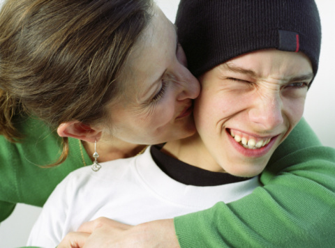 Mother kissing teenage boy (14-16) on cheek, close-up