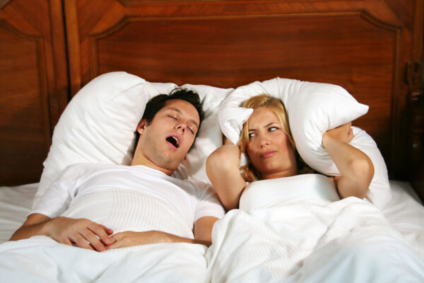 Couple in bed while the woman is trying to sleep and the man is snoring. Shutterstock