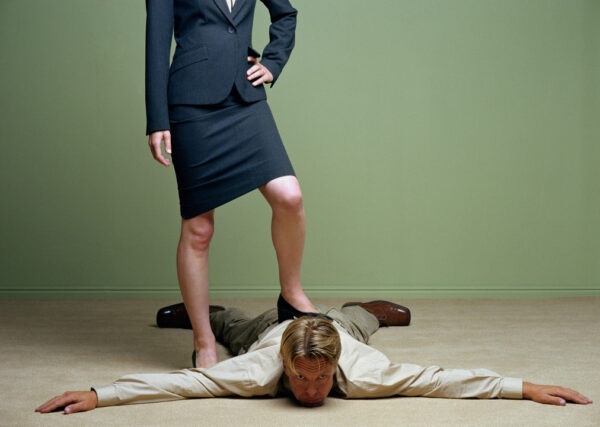 Woman standing with one foot on man spreadeagled on floor