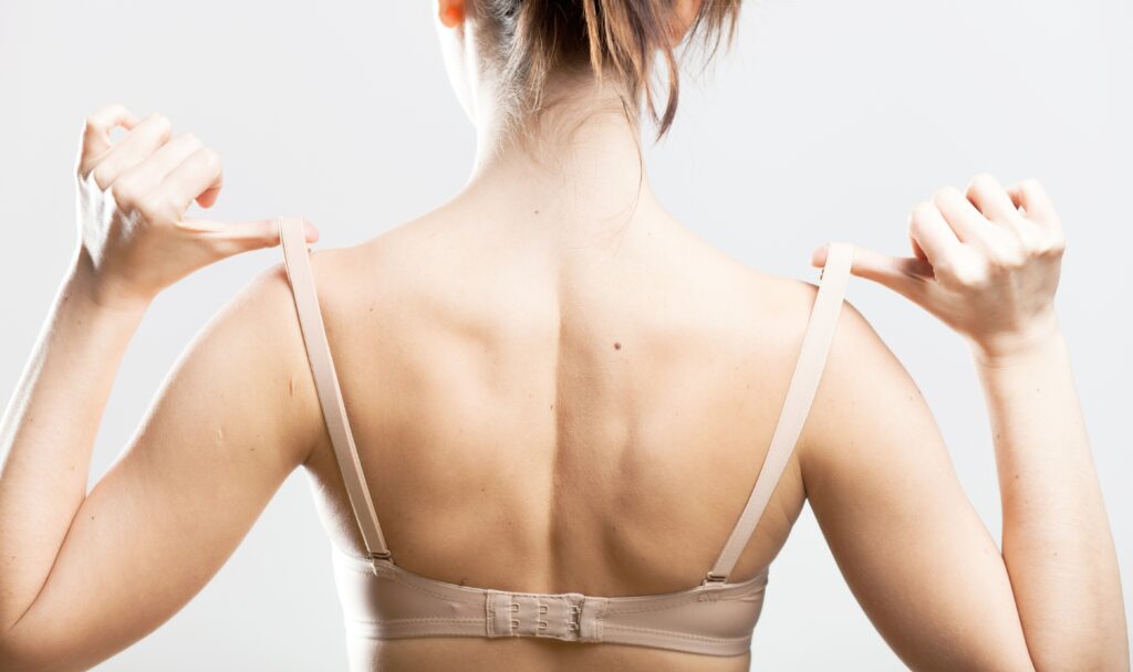 Woman holding a skin colored bra strap, closeup back view