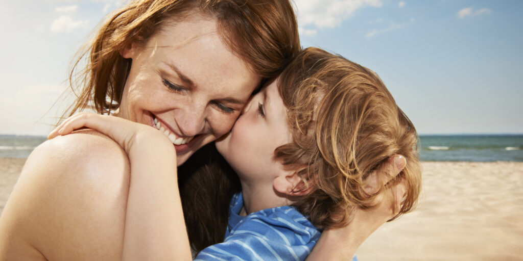Boy (4-5 years) kissing mother, smiling, close up