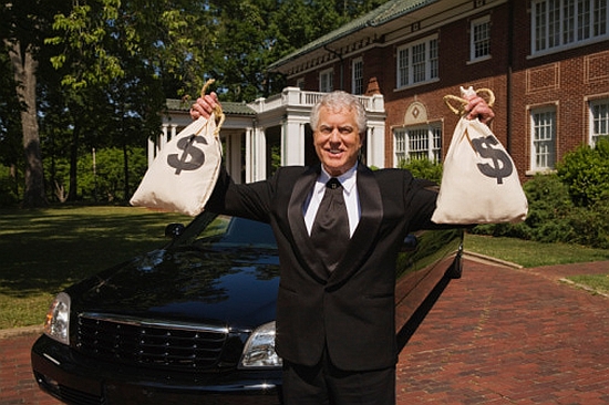 Man with money bags in front of mansion