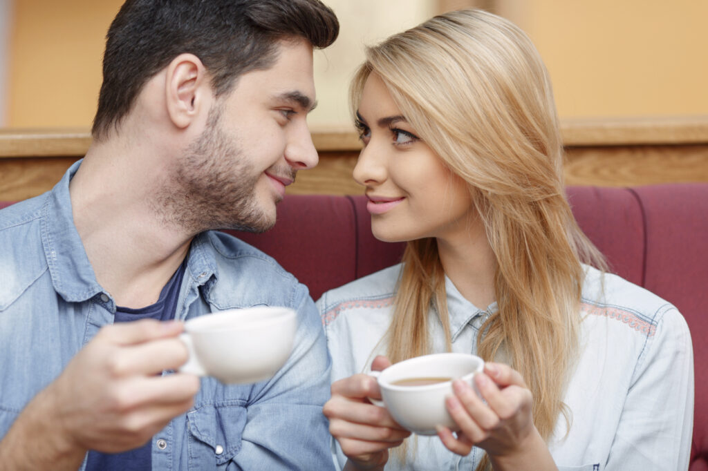 Enjoying fresh coffee together. Closeup of beautiful young couple looking at each other and smiling while enjoying coffee in cafe together
