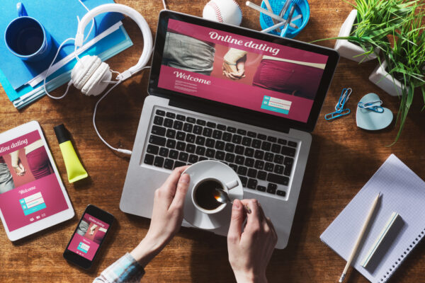 Online dating website on a laptop display, hardwood desktop and stationery on background