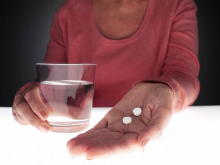 Woman holding pills and glass of water (close-up)