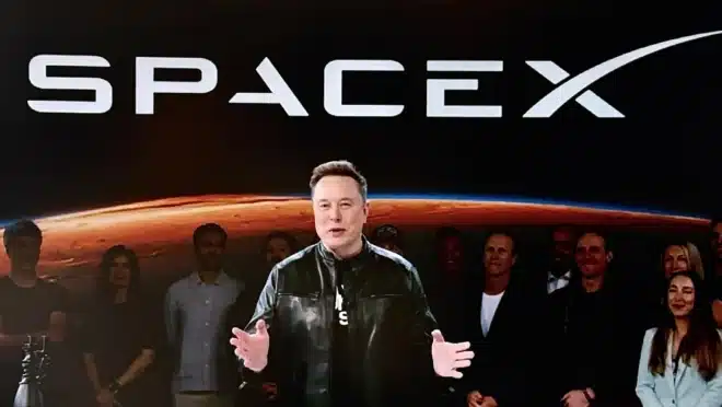 Elon Musk em frente ao logotipo da SpaceX com gráfico de alta ao fundo.